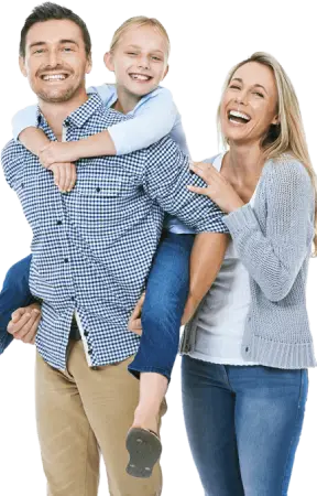 A smiling family: a woman stands beside a man carrying a child on his back, all dressed casually in a cheerful setting.